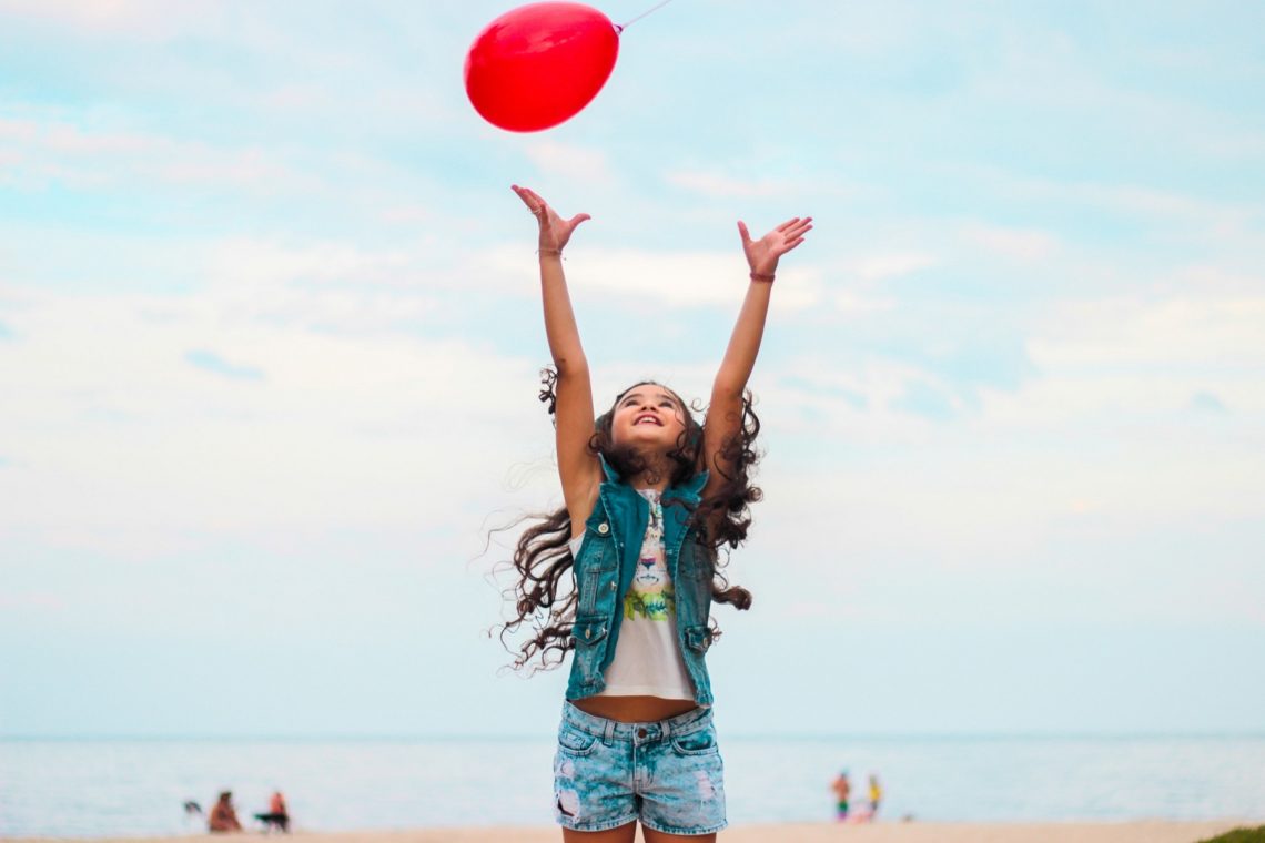 Une petite fille lance un ballon rouge dans le ciel