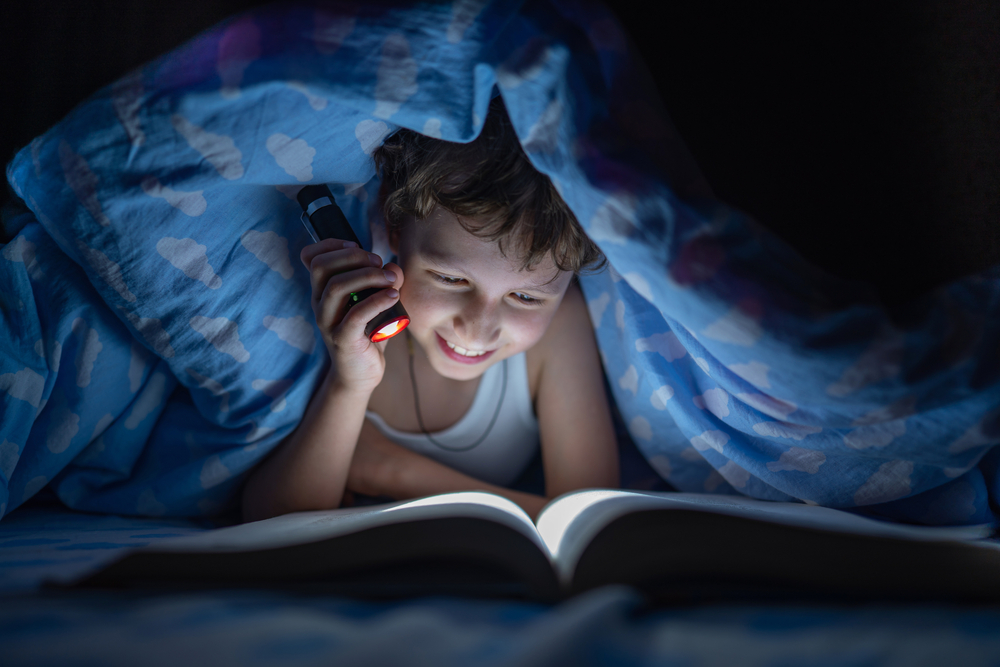 Un jeune garçon lit un livre sous sa couette