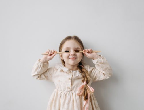 Une petite fille cache ses yeux avec des brosses à dent