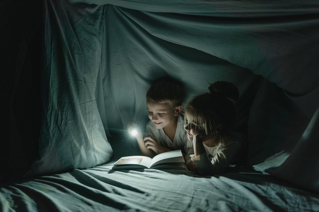 Deux enfants lisent une histoire sous la couette