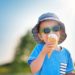 Un petit garçon mange une glace, il est protégé par un chapeau et des lunettes de soleil