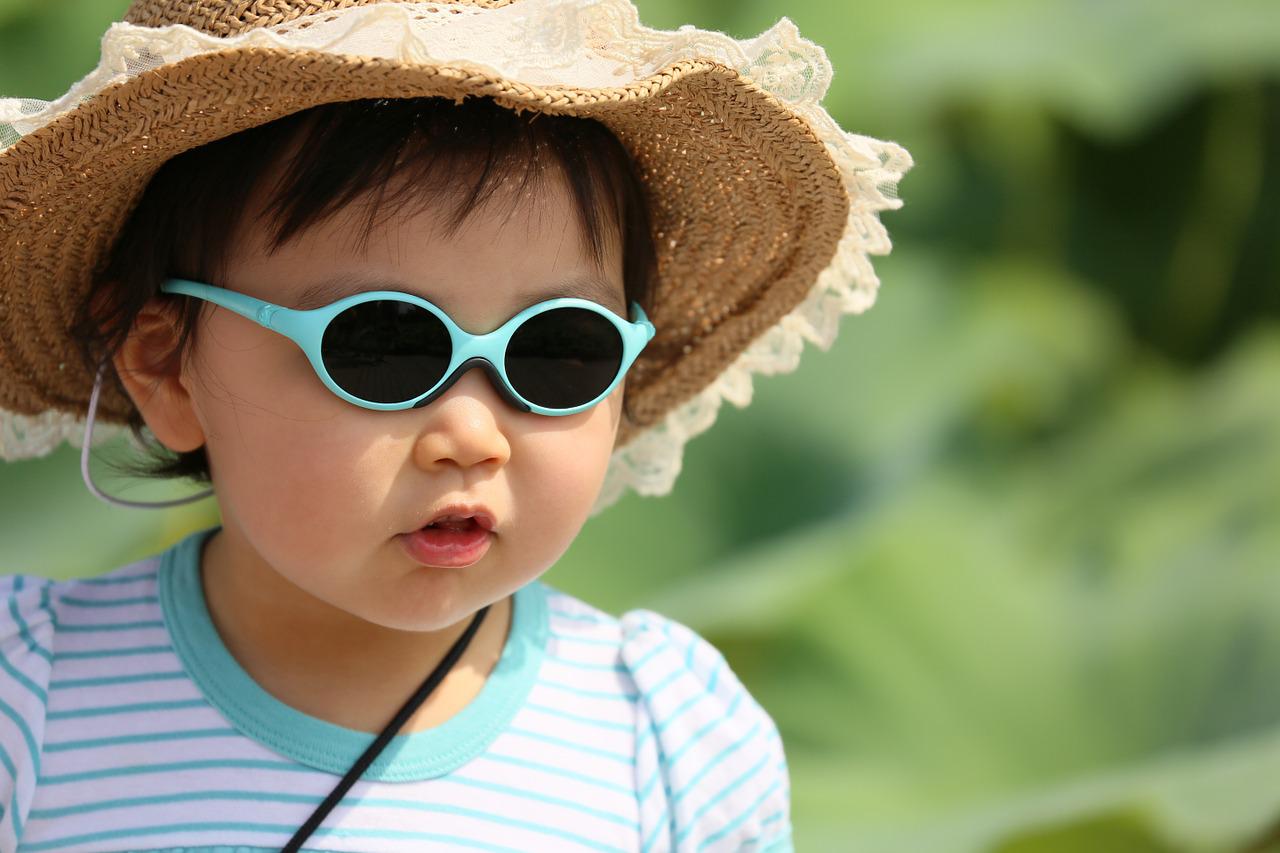 Une petite fille porte un chapeau de paille et des lunettes de soleil vertes