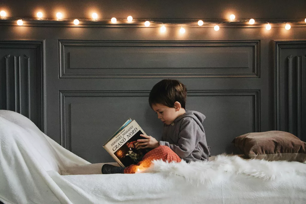 Un petit garçon découvre un livre assis sur son lit