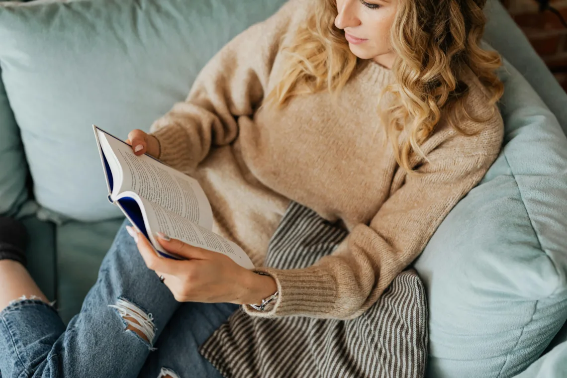 Adulte lisant un livre sur un canapé pour se détendre