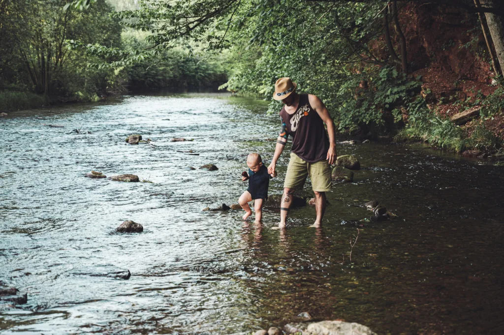Un papa et son petit garçon ont les pieds dans une rivière
