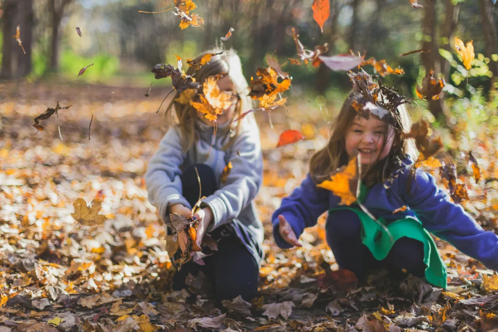 2 petites filles sautent dans un tas de feuilles mortes