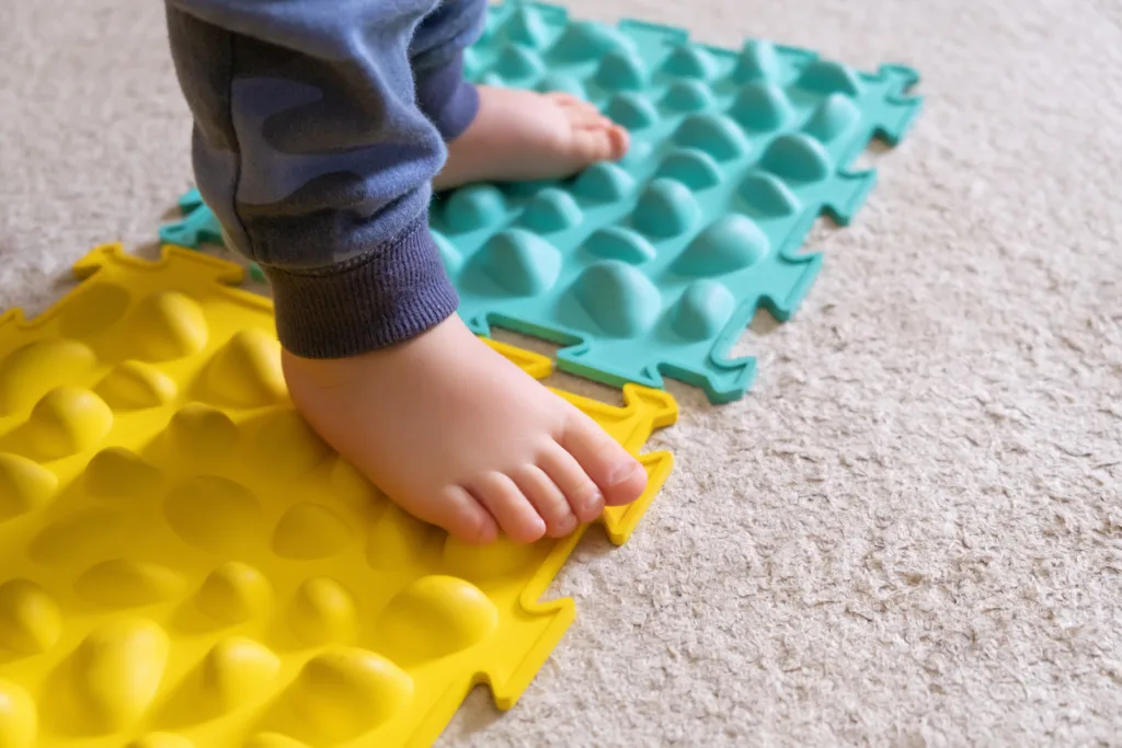 Un tout petit marche sur des bandes de couleur avec des formes : motricité fine